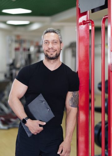 Daily sport routine, healthy lifestyle. Gray haired smiling coach man portrait in the gym