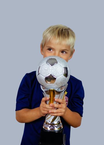 young-soccer-player-in-blue-jersey-holds-winners-cup-after-the-goal-isolated-at-light-background